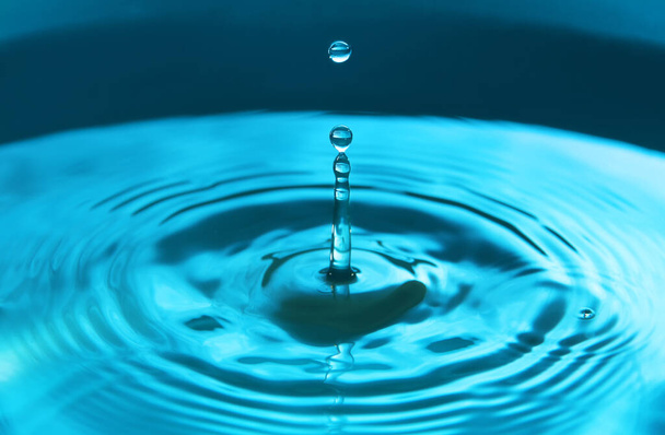 Vízcsepp esik a vízbe, így tökéletes koncentrikus körök. Absztrakt kék háttér. - Fotó, kép