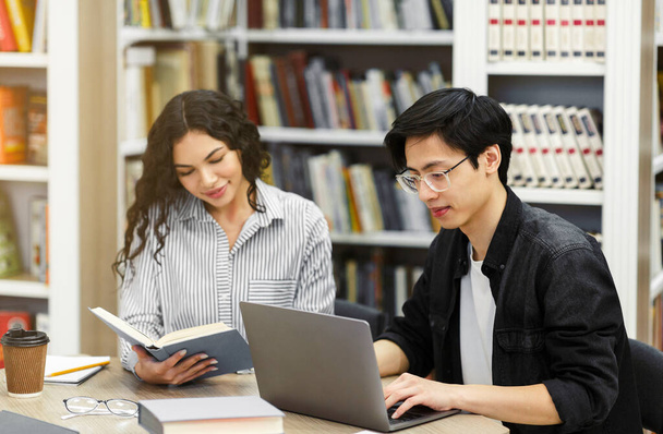 Twee lachende multiculturele studenten leren op de campus bibliotheek - Foto, afbeelding