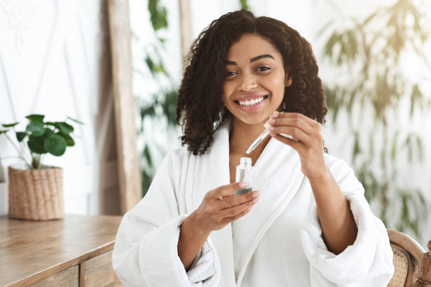 Afro Woman In Bathrobe Holding Organic Serum, Ready To Apply On Face - Фото, изображение
