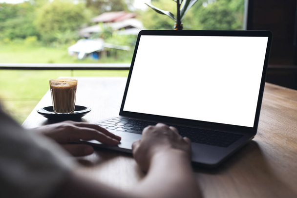 Mockup image of a woman using laptop with blank white desktop screen with coffee cup on wooden table  - Photo, Image