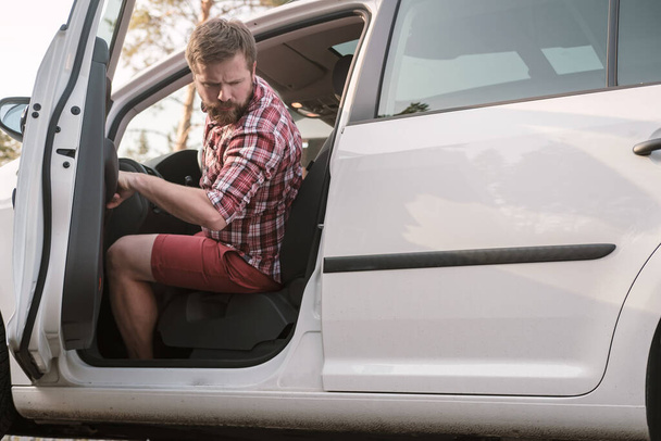 Ένας άνδρας οδηγός κάθεται πίσω από το τιμόνι ενός αυτοκινήτου με μια ανοιχτή πόρτα ένα - Φωτογραφία, εικόνα