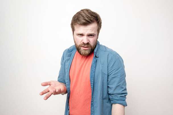 Caucasian bearded young man is baffled, looks confidently, gestures with his hand and tries to find out something. Negative emotions. Isolated on a white background. - Photo, Image