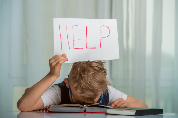 Gyerek fiú alszik egy tankönyvvel a feje felett és egy táblát tart a "Segítség" szóval. - Fotó, kép