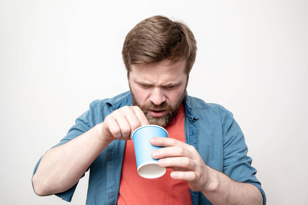 Bearded man with a paper cup in hand, in disgust, takes something out of the coffee he just drank. Negative emotions. Concept of spoiled products. - Foto, imagen
