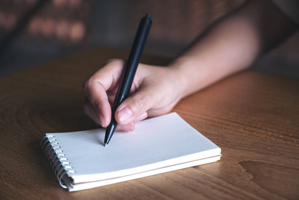 Nahaufnahme einer Hand, die auf ein weißes Blanko-Notizbuch auf einem Holztisch schreibt  - Foto, Bild