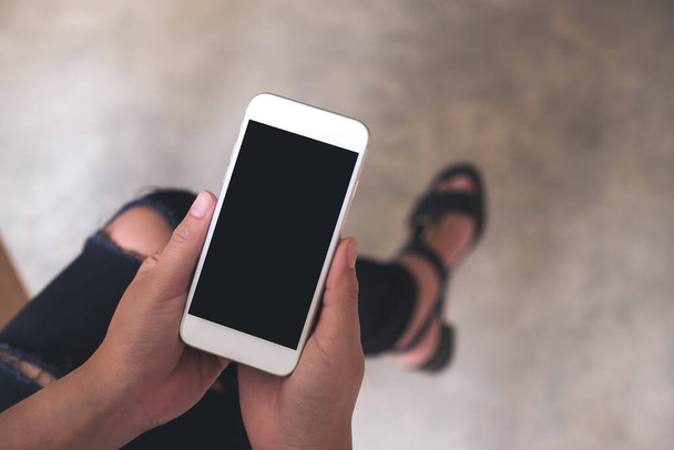 Visualizzazione dall'alto immagine mockup delle mani di una donna che tiene il telefono cellulare bianco con schermo nero vuoto sulla coscia
  - Foto, immagini