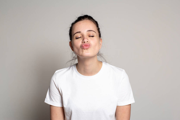 Beautiful young woman closed eyes and pouted lips in anticipation of a kiss. Funny portrait of a woman. Isolated on white background. - Foto, Imagen