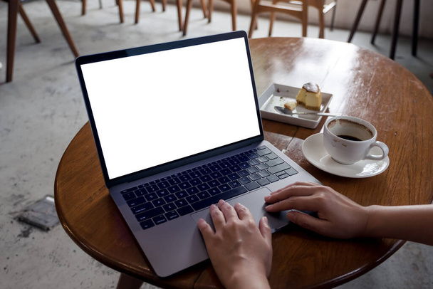 コーヒーカップ付きの白いデスクトップ画面とカフェで木製のテーブルの上にケーキとノートパソコンを使用して手のモックアップイメージ - 写真・画像