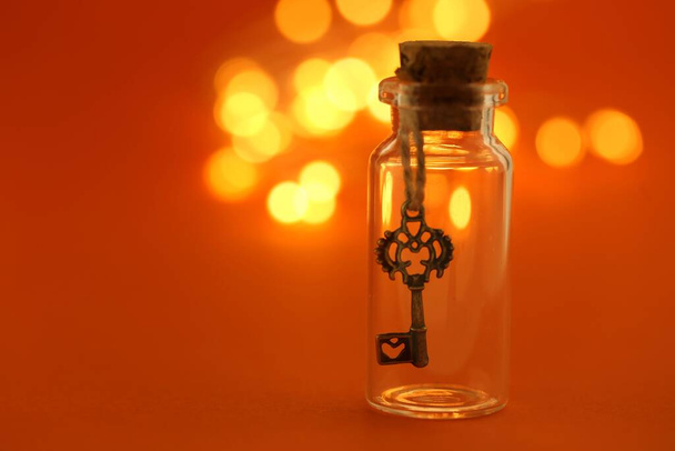 Key in a bottle with shining yellow bokeh on an orange background - Photo, Image