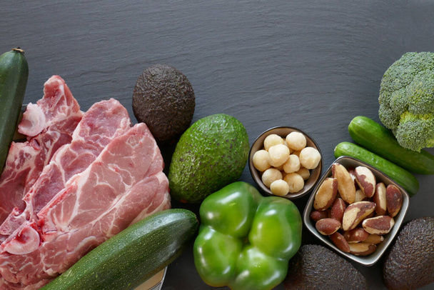 Dieta Keto. Aguacate, calabacín, pepinos, queso, carne, nueces sobre un fondo de pizarra negra
 - Foto, Imagen