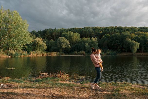 Mother and baby girl sitting near lake. Local travel. New normal vacation. Mothers day - Fotografie, Obrázek