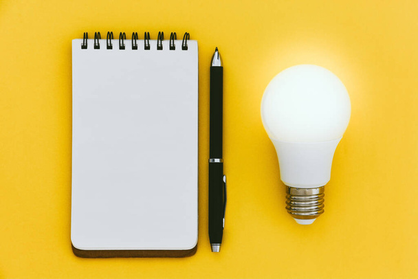 bovenaanzicht van lege open notebook, pen en LED-lamp op gele achtergrond met kopieerruimte, ideeënconcept, plat lay - Foto, afbeelding
