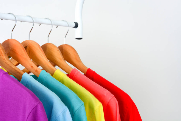 collezione da vicino di t-shirt colorate arcobaleno appese su appendiabiti in legno in armadio o portabiti su sfondo bianco, copiare lo spazio - Foto, immagini