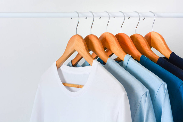 fermer la collection nuance de ton bleu t-shirts de couleur suspendus sur cintre à vêtements en bois dans le placard ou le porte-vêtements sur fond blanc avec espace de copie - Photo, image