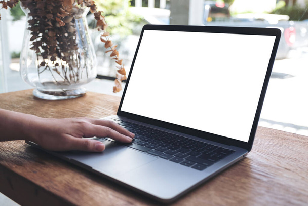 Mockup-Bild einer Hand mit Laptop und Berührung mit leerem weißen Desktop-Bildschirm auf Holztisch im Café - Foto, Bild