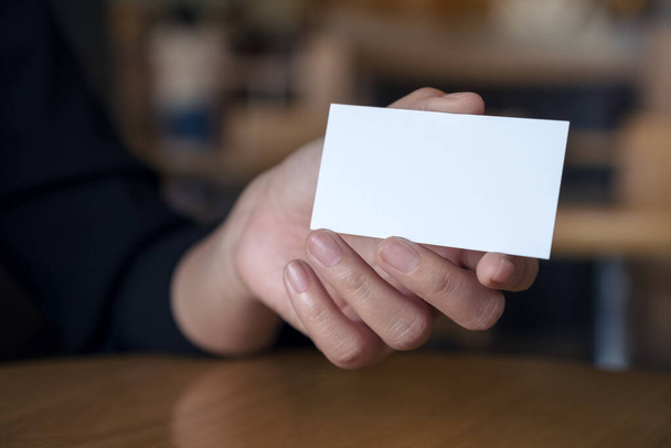 Mano de mujer sosteniendo y mostrando una tarjeta de visita vacía en la mesa en la oficina
 - Foto, Imagen