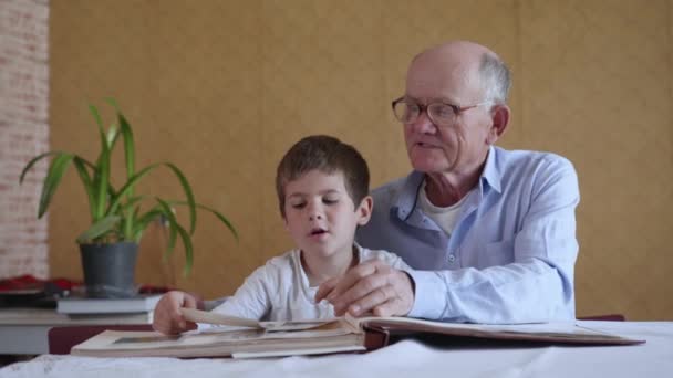Gözlüklü yaşlı büyükbaba oğlanla birlikte sevimli. Mutlu anıların keyfini çıkar. Geçmiş yılların anılarını anlat ve aile fotoğrafı albümünü izle. - Video, Çekim