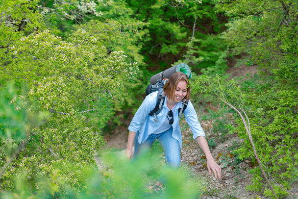 Mujer sonriente trepando por un sendero de montaña. Plantas y árboles en el fondo. Deportes activos y turismo
. - Foto, Imagen