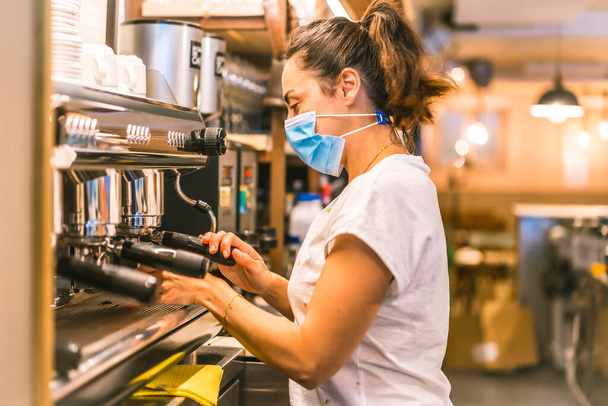A waitress with a face mask in a bar. New normality, security measures after the coronavirus pandemic, social distance, covid-19. Preparing a coffee - Fotoğraf, Görsel