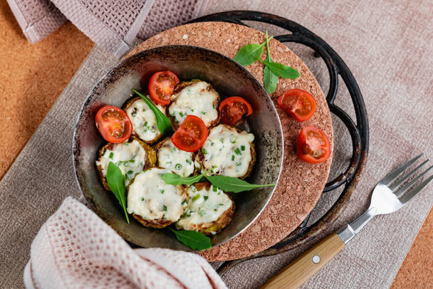 Pan-fried zucchini with garlic sauce and cherry tomatoes. Next to arugula, napkins, fork and mayonnaise. A colorful appetizer dish in a rustic setting - Фото, зображення
