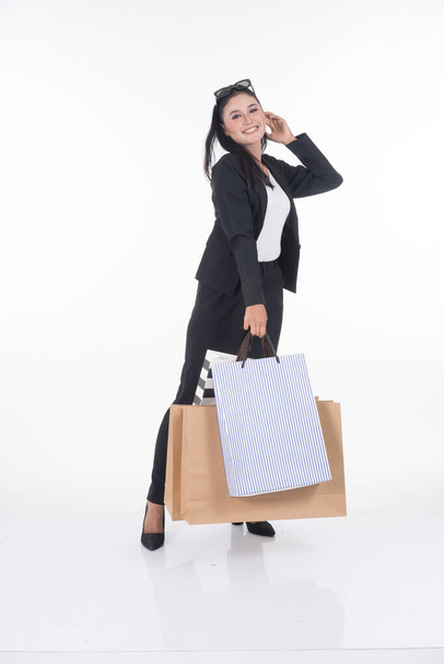 A beautiful Asian woman wearing officewear poses with shopping bags isolated on white background. Full body suitable for image cut out and manipulation works for business and commerce concepts. - Photo, Image