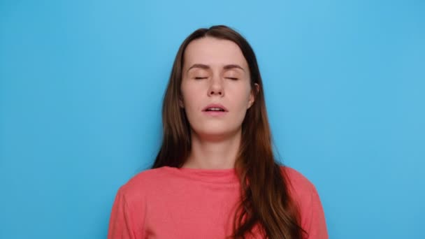 Portrait of cute woman having sleepy expression looking tired holding her hand on cheek closing her eyes, wears red sweater, isolated on blue studio background. People, healthy peaceful sleep concept - Filmati, video