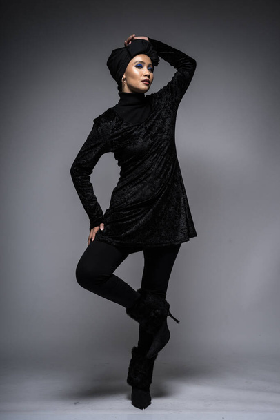 Высокомодный портрет азиатки в черном топе и брюках с тюрбаном на сером фоне. Модная назидательная концепция для моды хиджабов. Полная длина
 - Фото, изображение