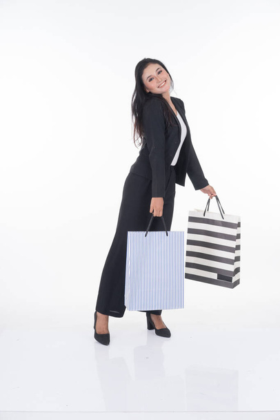 Μια όμορφη Ασιάτισσα που φοράει ρούχα γραφείου ποζάρει με τσάντες για ψώνια απομονωμένες σε λευκό φόντο. Πλήρες σώμα κατάλληλο για την εικόνα κοπεί και χειραγώγηση έργα για τις επιχειρήσεις και το εμπόριο έννοιες. - Φωτογραφία, εικόνα