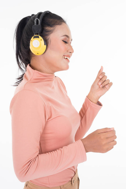 Веселий азіатський підліток, одягнений у халат і штани, використовуючи бездротові навушники, які насолоджуються слуханням музичного портрету, вирізаного на білому тлі. Легко відрізати. Портретна орієнтація. - Фото, зображення