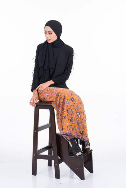 Beautiful female Asian model in various poses wearing a black top with batik sarong and hijab isolated on white background. Beauty and hijab fashion concept. Full length portrait - Photo, Image