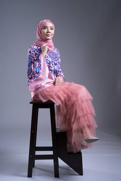 Full length πορτρέτο ενός όμορφου γυναικείου μοντέλου που φοράει παραδοσιακό φόρεμα και χιτζάμπ, ένα lifestyle ένδυμα για μουσουλμάνες γυναίκες σε γκρι φόντο. Idul Fitri και χιτζάμπ έννοια μόδας. - Φωτογραφία, εικόνα