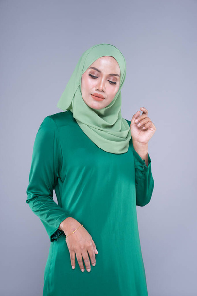 Beautiful female model in modern kurung and hijab, a modern lifestyle apparel for Muslim women isolated on grey background. Beauty and hijab fashion concept. Half length portrait - Photo, Image