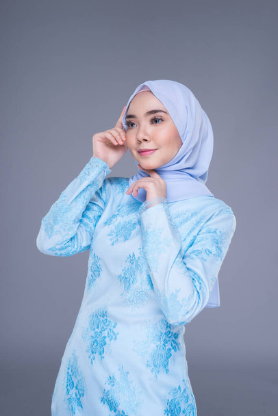 Mooi moslim vrouwelijk model met pastelblauw moderne kurung met hijab, een urban lifestyle kleding voor moslimvrouwen geïsoleerd op grijze achtergrond. Schoonheid en hijab mode concept. Halve lengte - Foto, afbeelding