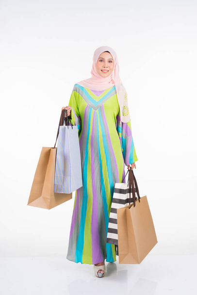 Un modello femminile musulmano bello e felice in un abito tradizionale kaftan / caftano che trasporta borse della spesa isolate su sfondo bianco. Eidul fitri moda e preparazione festiva shopping concept
 - Foto, immagini