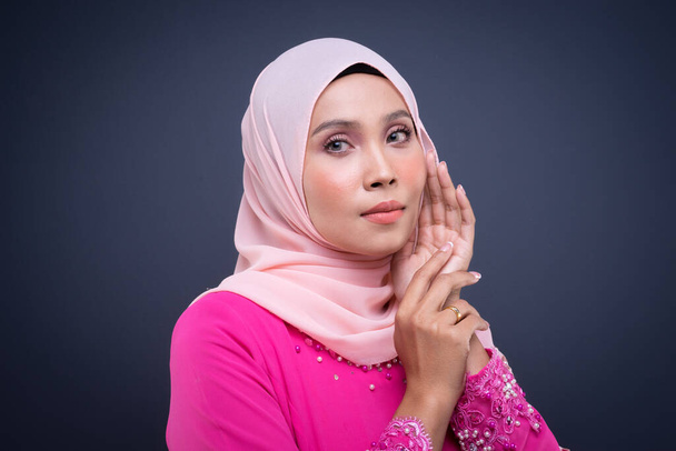 Kopfballporträt eines schönen muslimischen Models, das rosa Kurung mit Hijab trägt, einer modernen urbanen Lifestylebekleidung für muslimische Frauen, isoliert auf grauem Hintergrund. Schönheits- und Hijab-Modekonzept. - Foto, Bild