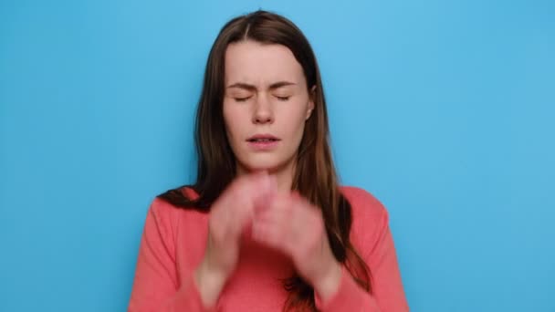 Stressful unhappy young woman with headache, holding her hands on head, sad anxious girl concerned about health problems suffer from migraine, wears re sweater, isolated on blue studio background - Filmati, video
