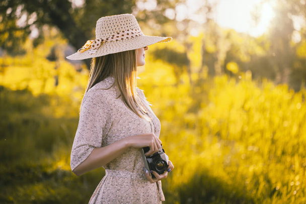 girl photographer in a sunny meadow with a retro camera takes a photo of the landscape - Foto, imagen