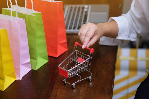 İnternet alışveriş konsepti için dizüstü bilgisayarı olan kadın ve küçük alışveriş arabası - Fotoğraf, Görsel
