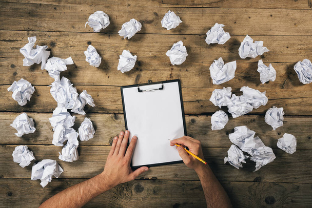 Hands holding clipboard and write Mock-up or ideas with a pen surrounded from crumpled paper balls. Brainstorming Concept image - Фото, зображення