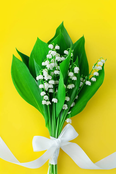 Lily z doliny kwiat bukiet & biały bowknot na żółtym tle zbliżenie, piękne lilie kilka i zielone liście z wstążką, convallaria majalis, romantyczna kartka okolicznościowa, jasny wzór kwiatowy - Zdjęcie, obraz