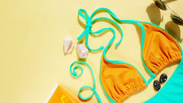 Orange swimsuit, sunglasses, sunblock, seashells on yellow background. Summer vacation concept. Flat lay, top view. Copy space - Foto, Imagen