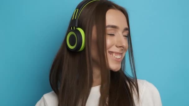 Atrakcyjna kobieta na mocnym tle w stylowych zielonych słuchawkach słucha muzyki i uśmiecha się do kamery. Aktywny tryb życia - Materiał filmowy, wideo