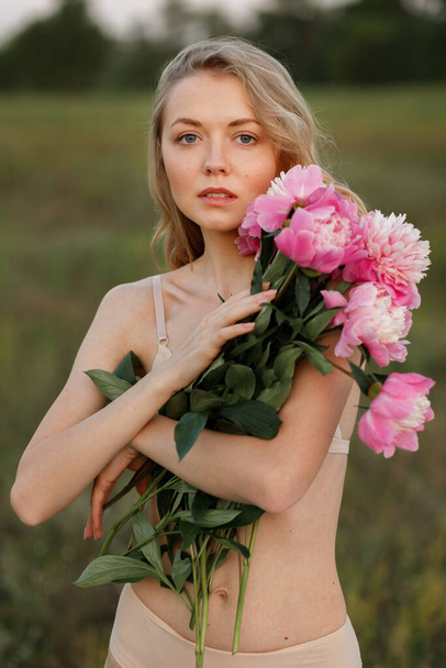 Blonde with blue eyes in beige lingerie holds pink flowers - Φωτογραφία, εικόνα