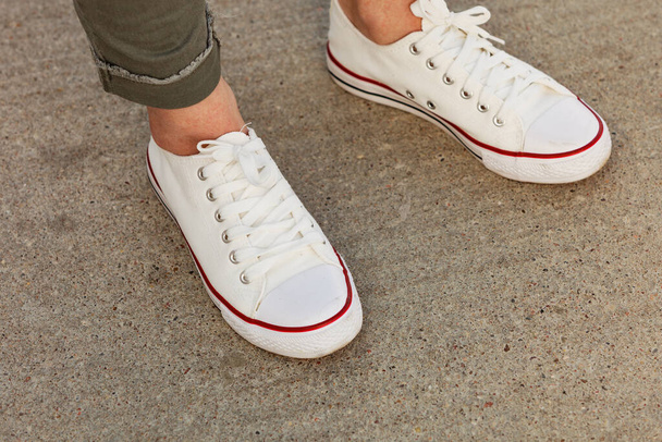 Woman feet wearing white sneakers, casual shoes. Female relaxing outdoors. Footwear perfect for warm weather. - Foto, Bild
