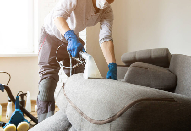 Man cleaning sofa chemical cleaning with professionally extraction method. Upholstered furniture. Early spring cleaning or regular clean up. - Φωτογραφία, εικόνα