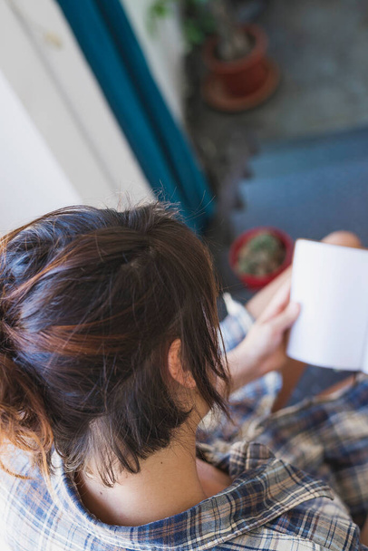 Boven het zicht van een jonge vrouw zittend op de trap naar huis terwijl ze een boek leest - Foto, afbeelding