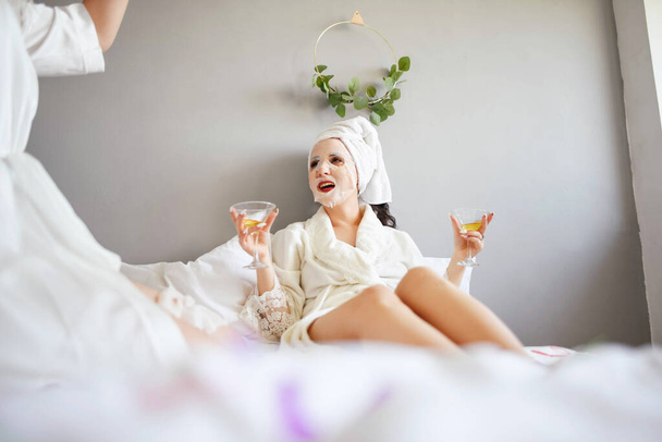 Novias con máscaras en la cara beben champán mientras yacen en la cama
. - Foto, imagen