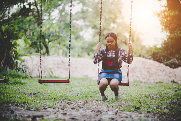 Jovem menina feliz montando em um balanço no parque
 - Foto, Imagem
