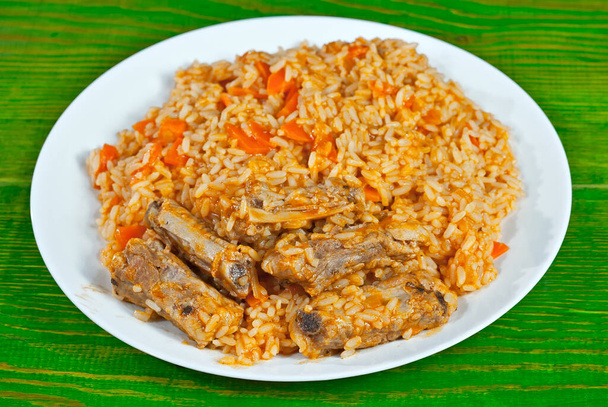 Pilaf with meat and carrots in a white plate. Rice on an old green board. - Photo, Image