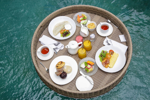 Schwimmendes Frühstück, ein großes Tablett im Pool, komplette Mahlzeit am Morgen mit frischem Kaffee, warmem Brot, Gewürzen und Säften - Foto, Bild